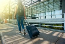 A woman walks with a suitcase outside an airport terminal, ready for travel.